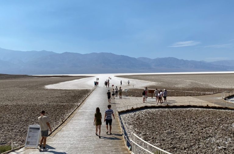 Walkway through arid landscape with people enjoying the view of mountains in the distance.
