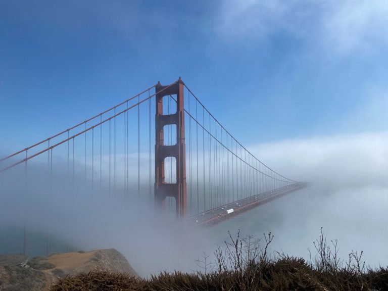 Golden Gate Bridge partially enveloped in fog against a clear blue sky.