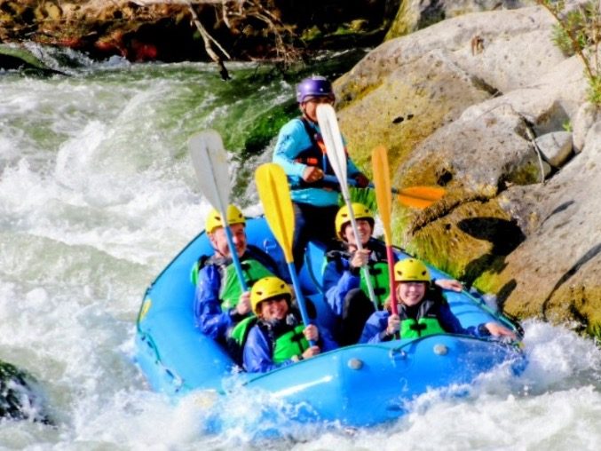 Group of five people in a blue raft navigating a river with paddles.