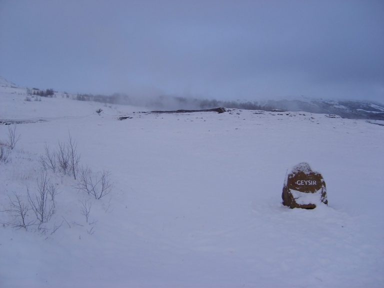 A snowy landscape with low hills and a single rock in the foreground.