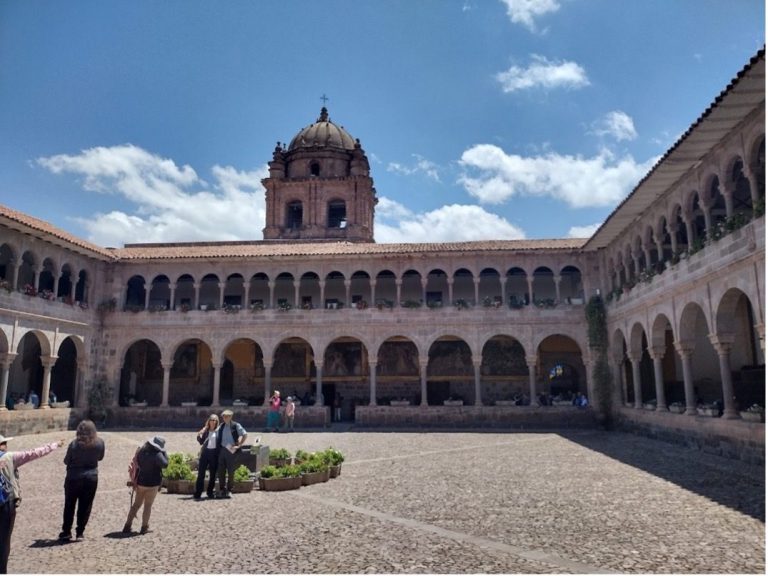 Courtyard of a historical building with arches and a domed tower under a blue sky.