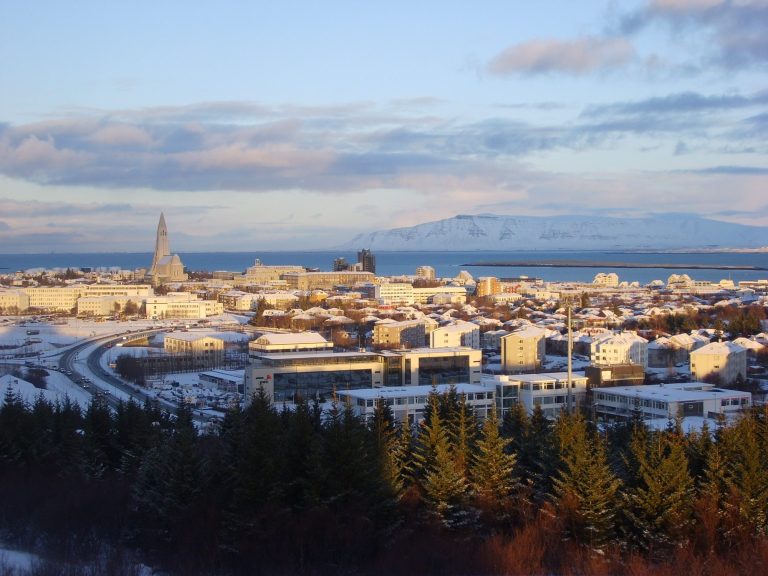 Snow-covered cityscape of Reykjavik with distant mountains under a clear blue sky.