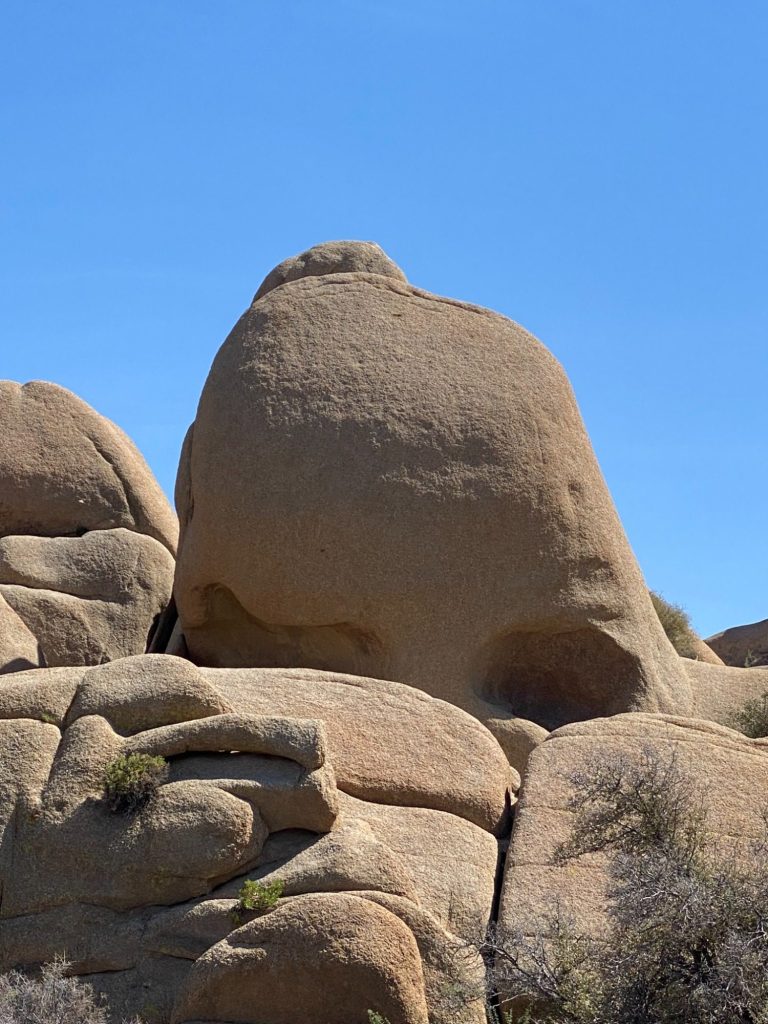 Large, rounded rock formation against a clear blue sky in a desert landscape.