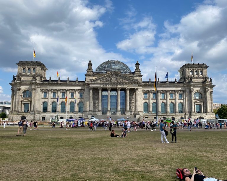 Historic Reichstag building with a glass dome, surrounded by people on the lawn.