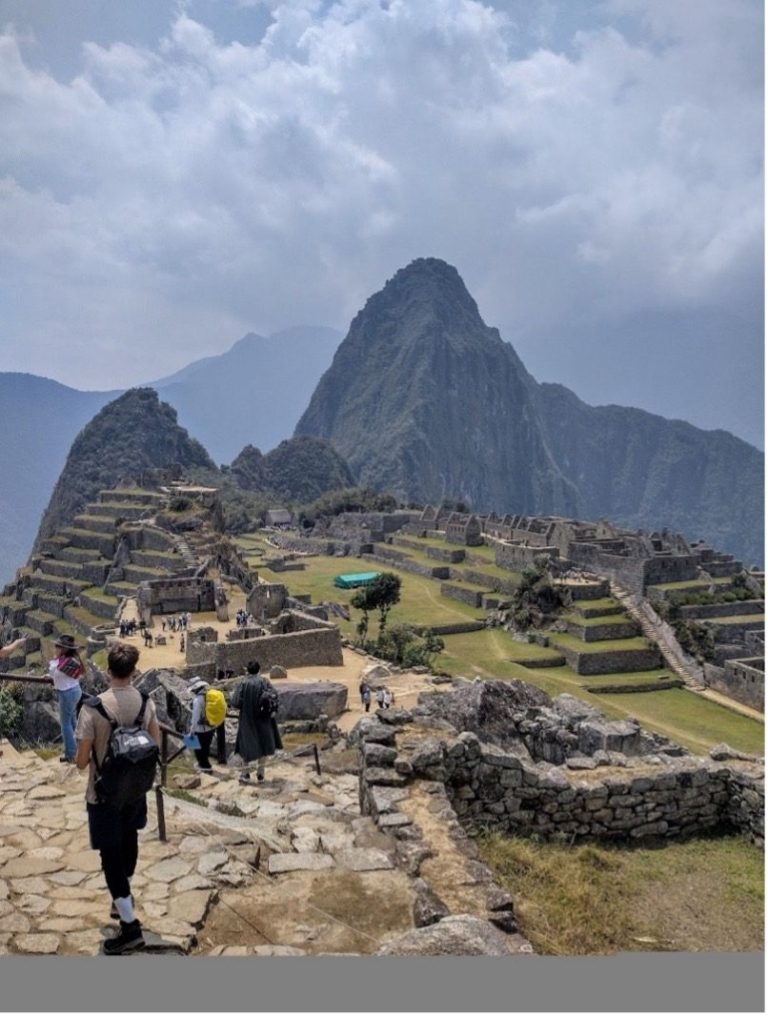 Visitors walking through the ancient ruins of Machu Picchu with mountains in the background.