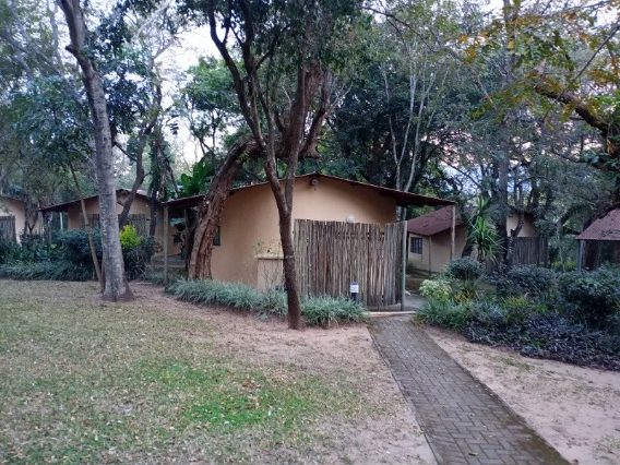 A pathway leading to a wooden gate, surrounded by greenery and rustic buildings.