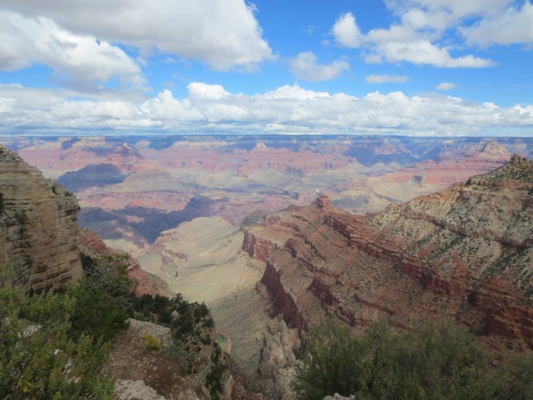 Vast view of the Grand Canyon with layered rock formations and a blue sky.