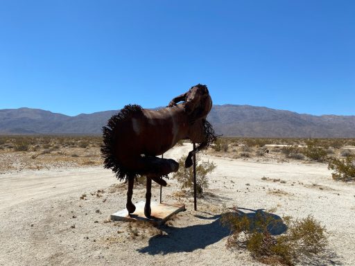 A large horse sculpture stands in a desert landscape under a clear blue sky.