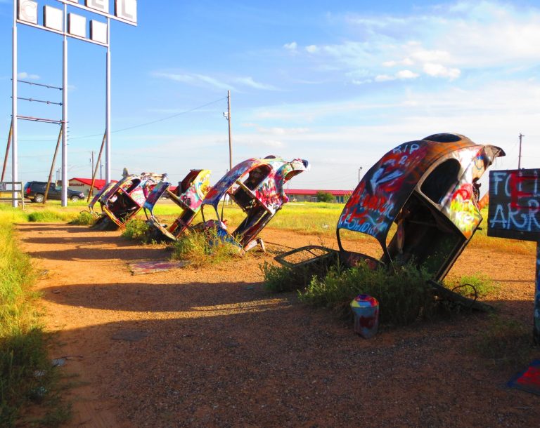 Several colourful, graffiti-covered cars are partially buried in grassy ground.