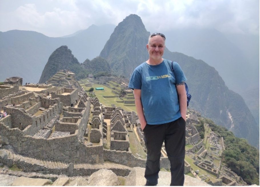 Person standing at Machu Picchu with ancient ruins and mountains in the background.