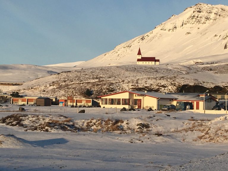 Snow-covered landscape with a church on a hill and buildings in the foreground.