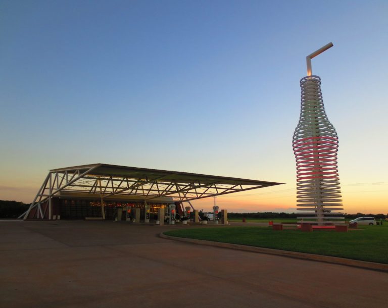 Coca-Cola bottle structure beside a modern pavilion at sunset.
