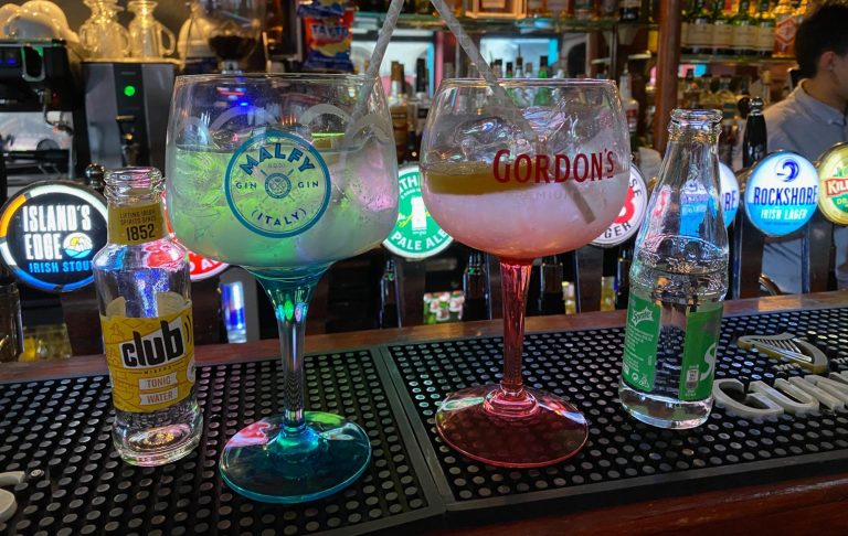 Three cocktails in large glasses on a bar counter, with vibrant colours and garnishes.