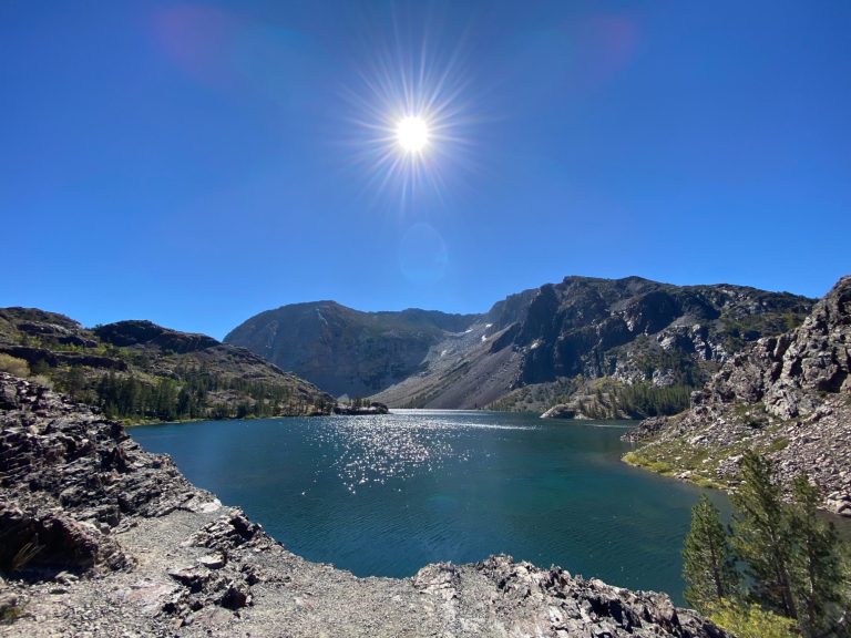 Scenic lake surrounded by mountains under a clear blue sky and a bright sun.