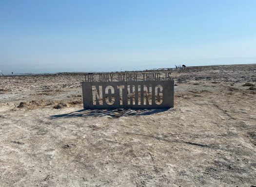 A weathered sign reading "NOTHING" on a barren landscape under a clear blue sky.