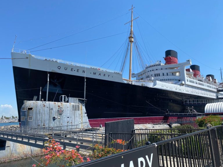 Historic ocean liner docked, showcasing its prominent black hull and red accents.