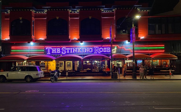 Exterior of a lively restaurant with vibrant neon signage in a city setting at night.