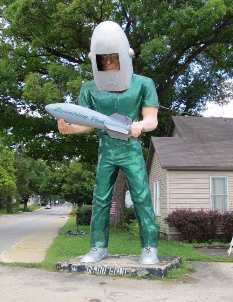 A large statue of a man in a helmet holding a rocket, wearing green attire.