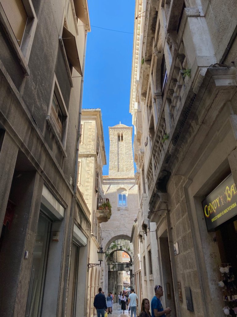 Street of the Old Town Narrow street view with tall buildings and a bell tower in the distance under a clear blue sky.
