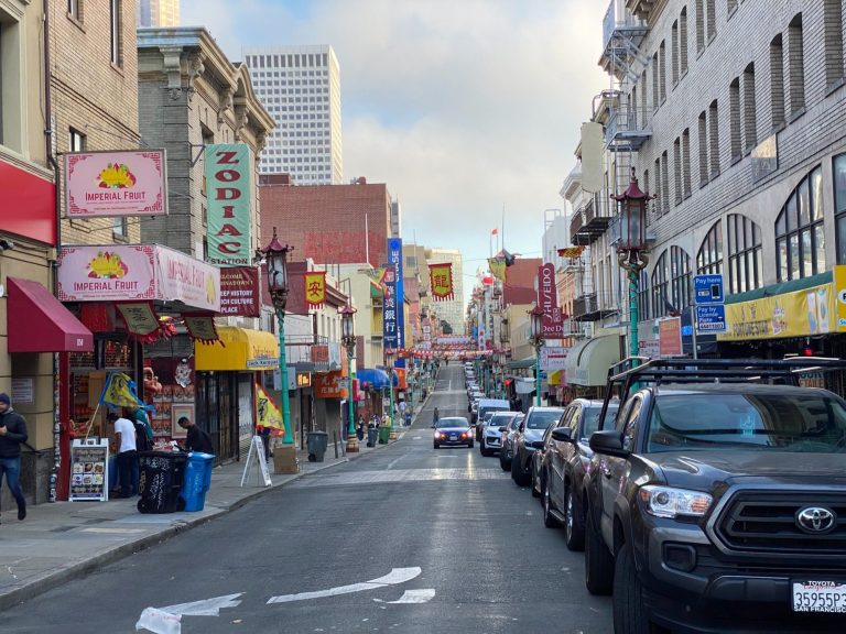 Colourful street scene in a vibrant urban area with shops and parked cars.