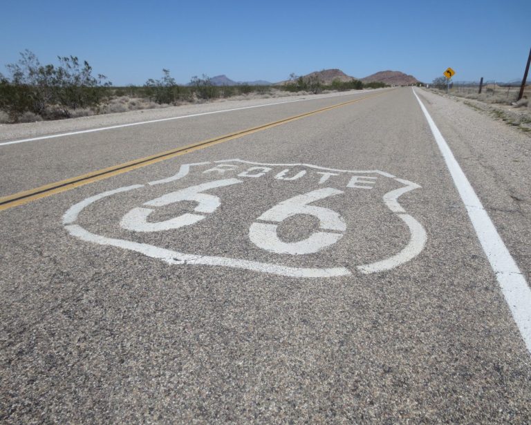 Route 66 highway sign painted on a deserted road with a clear blue sky.