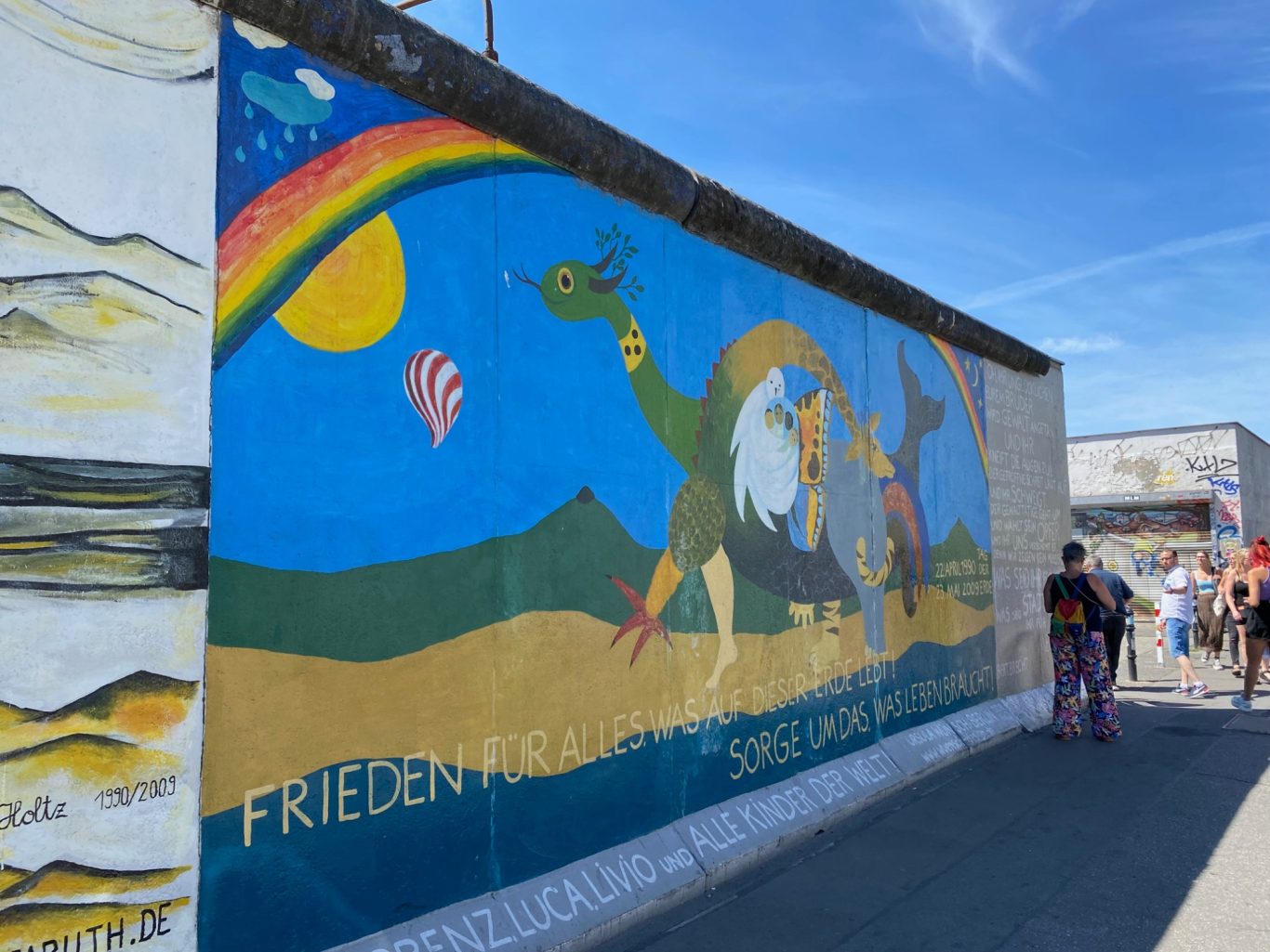 Frieden für Alles (Peace for Everything) Colourful mural depicting a dragon and other imagery, with a bright blue sky backdrop.