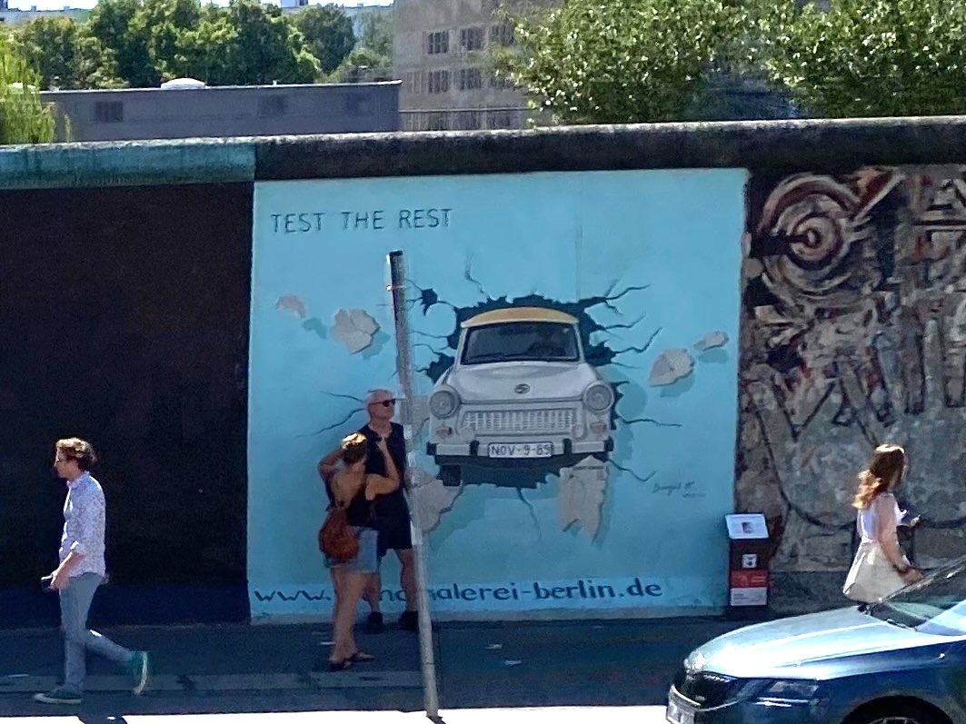 Test the Rest or The Trabant Mural of a yellow taxi breaking through a wall, with people walking by.