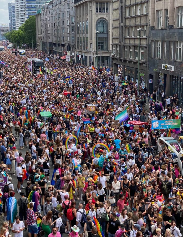 Berlin Pride 2022 Crowd at a vibrant pride parade with rainbow flags and banners lining the streets.