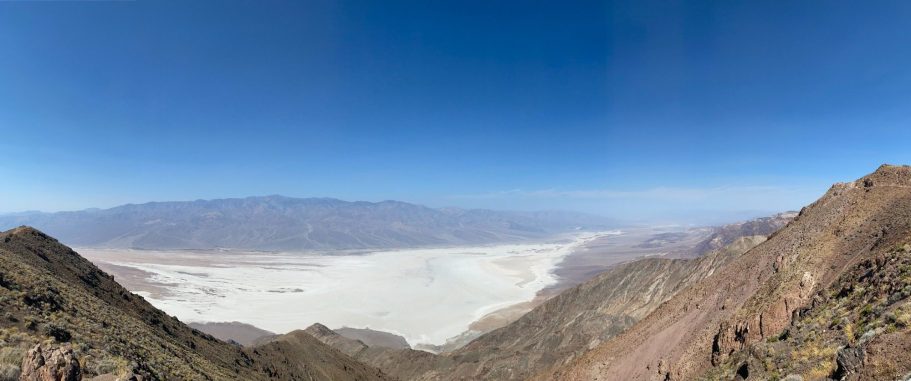 Panoramic view of a desert valley with mountains and a hazy blue sky.