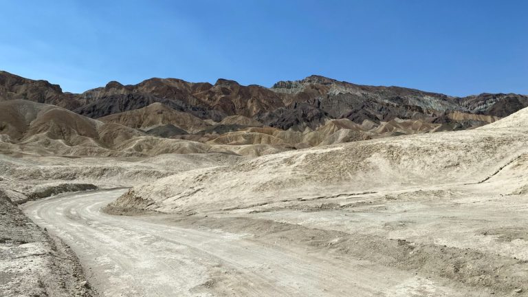 A dry, rocky landscape with sandy terrain and a clear blue sky above.