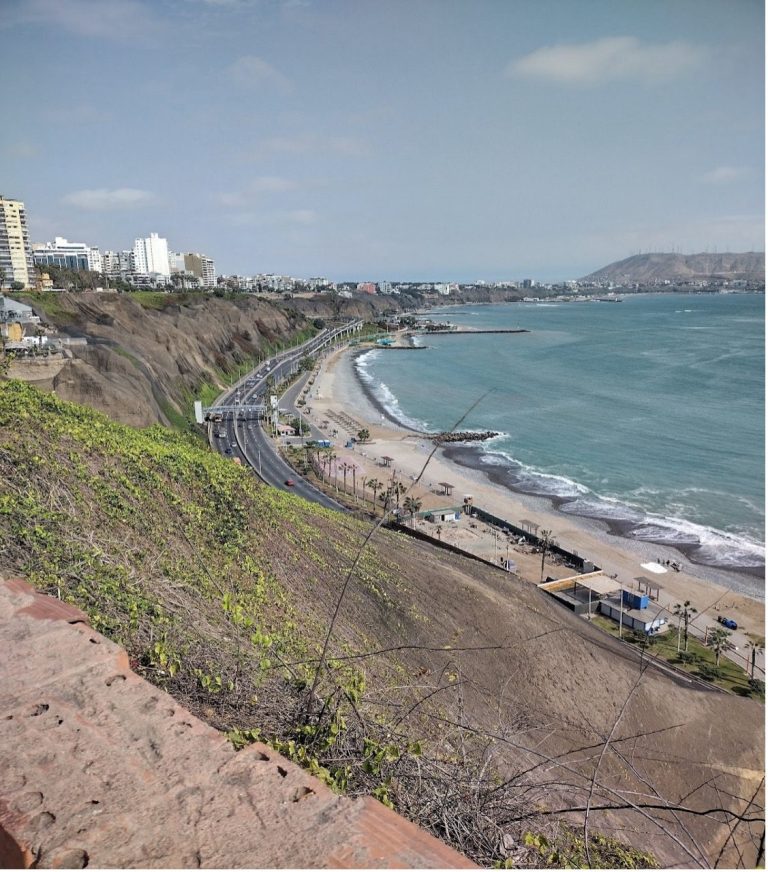 Coastal view with a road along the shore and buildings in the distance.