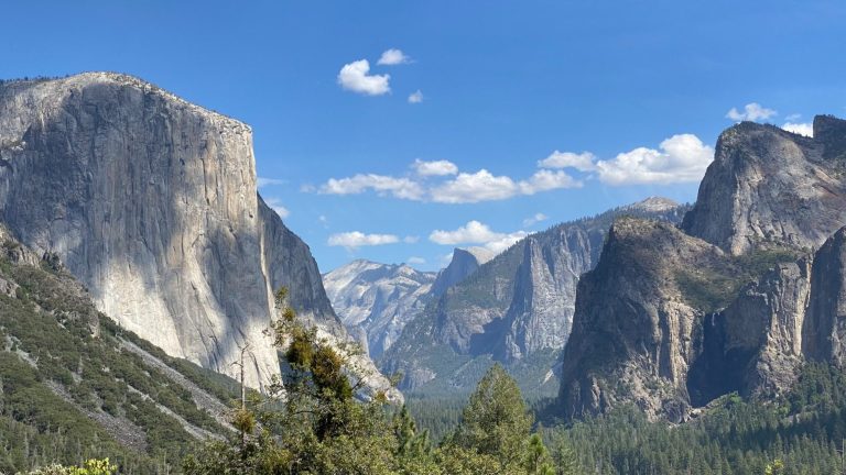 A panoramic view of Yosemite National Park featuring tall granite cliffs and a clear blue sky.