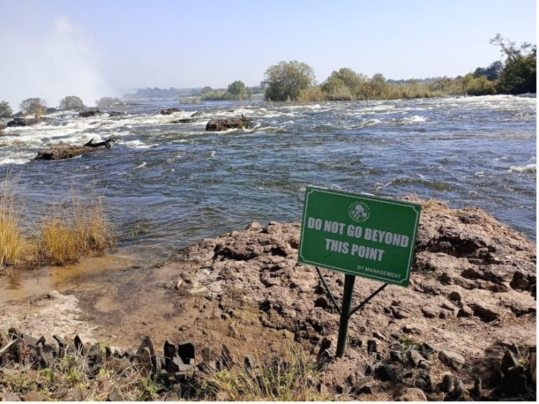 A river scene with a warning sign against swimming near rocky banks.