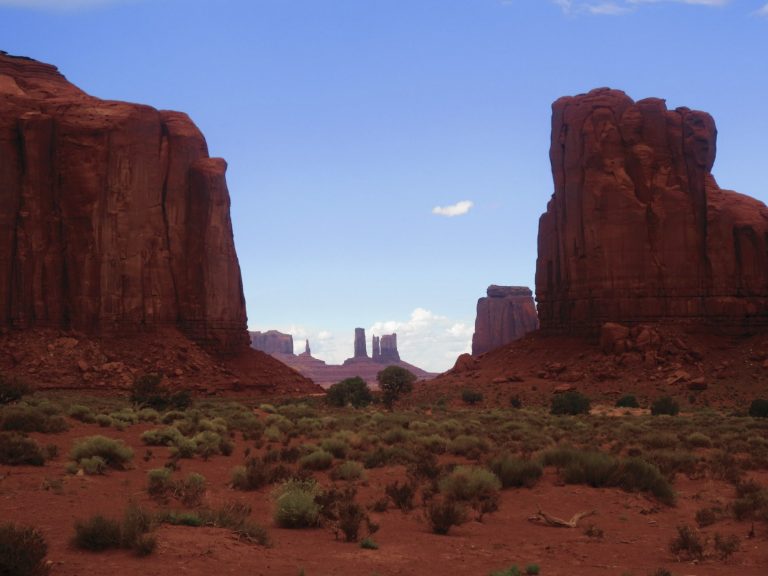 Red rock formations and a wide, open valley under a blue sky with scattered clouds.