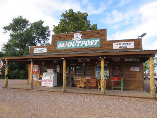 Wooden building marked “Outpost” with signs and a small porch, set in a rural area.