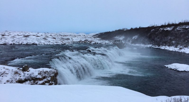 Snowy landscape with a waterfall cascading into a river, surrounded by icy terrain.