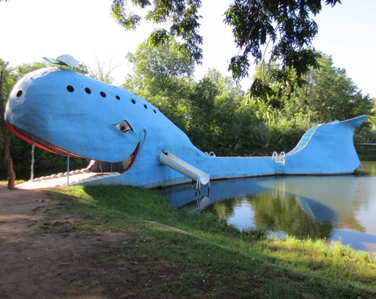 Blue whale-shaped structure by a pond, with trees in the background.