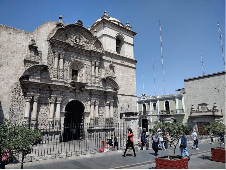 Historic building with ornate façade, surrounded by pedestrians and greenery.