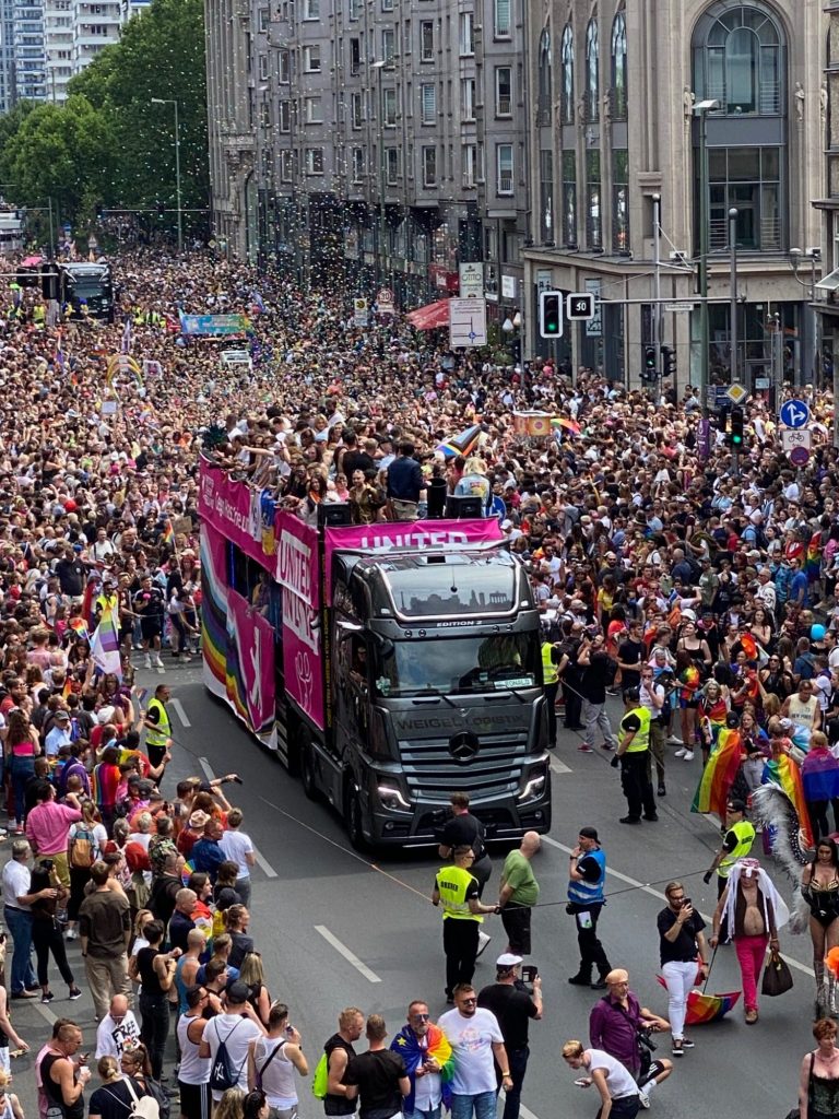 Berlin Pride 2022 A large crowd at a parade with a pink double-decker bus leading the festivities.