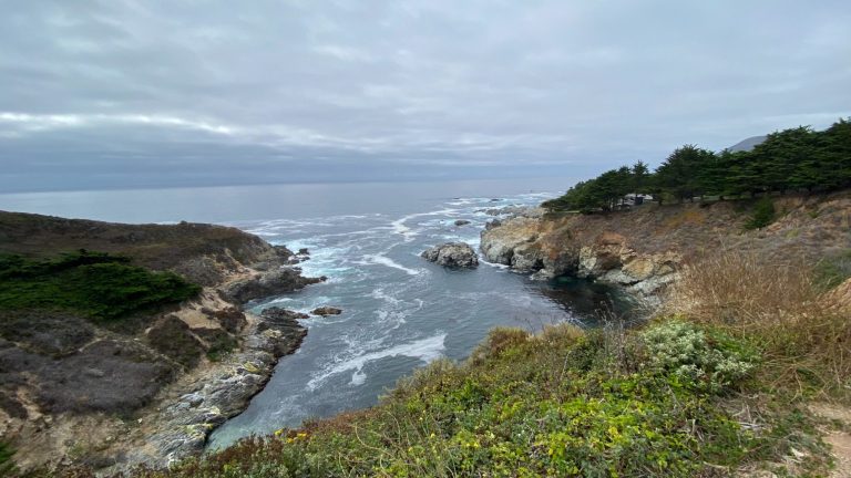 Coastal view with waves crashing against rocky cliffs under a cloudy sky.