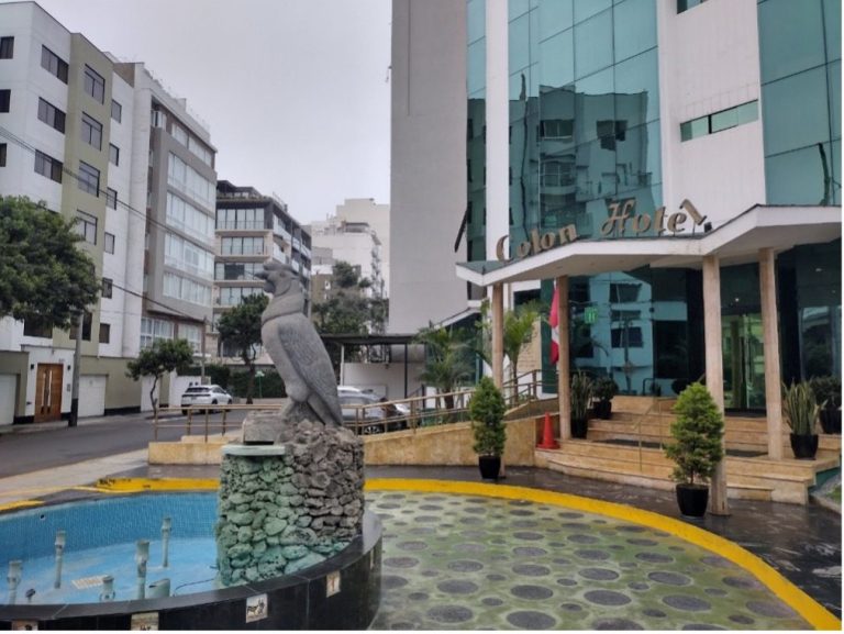 A statue of a bird in front of a modern building with greenery and a fountain.