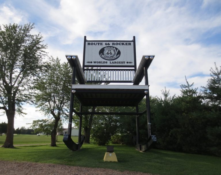 Large sign for a business, elevated on a platform amid trees and blue sky.