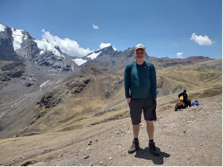 Person standing on a rocky mountain terrain with snowy peaks in the background.