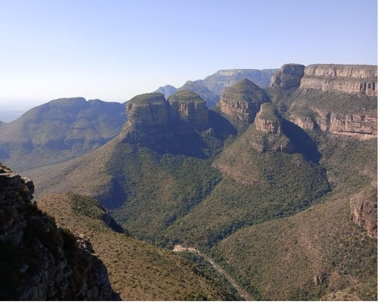 Mountainous landscape with lush greenery and rocky peaks under a clear blue sky.