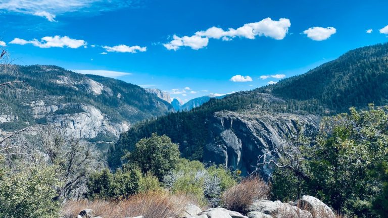 Panoramic view of mountains and valleys under a bright blue sky with scattered clouds.