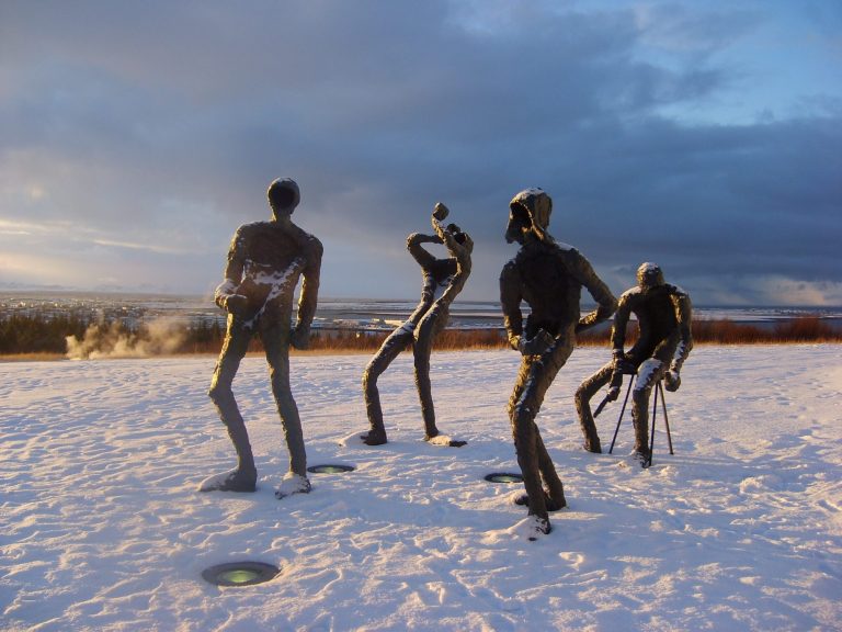 Four bronze sculptures standing on snow, with a dramatic sky in the background.