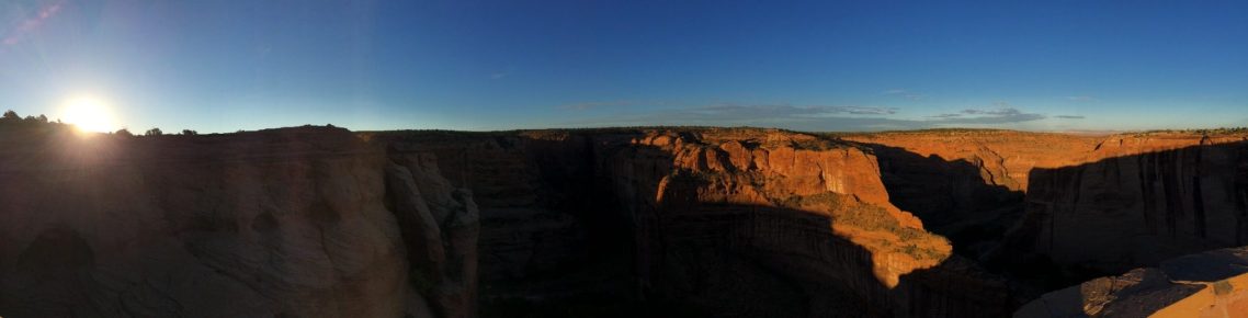 Panoramic view of a canyon at sunset, with warm hues illuminating the rocky landscape.