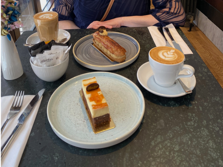Coffee, a slice of cake, a tart, and a dessert on plates at a café table.