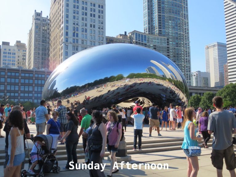 Crowd gathered around the reflective Cloud Gate sculpture in a sunny urban park.