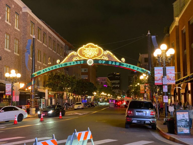 Night view of a lit arch sign welcoming visitors to a bustling urban area.